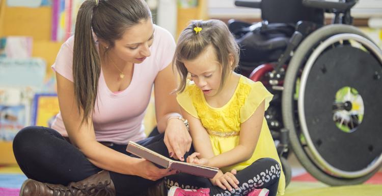 A woman sits on the ground with a child, who is reading from a book